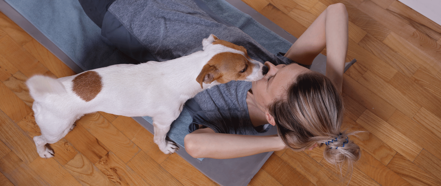 Dog an sniffing owner's face, who is lying on yoga mat.