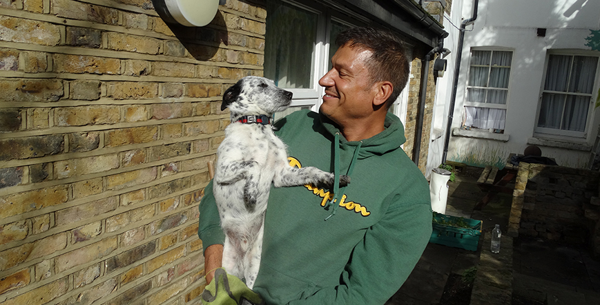 Man in a green jumper staring lovingly at the dog in his arms