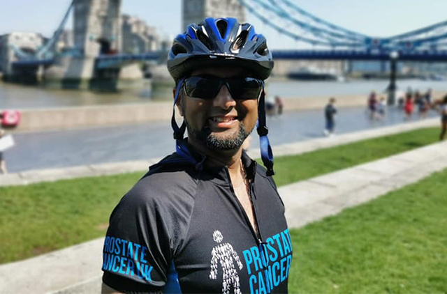 Man smiling in his bike helmet and jersey by Tower Bridge