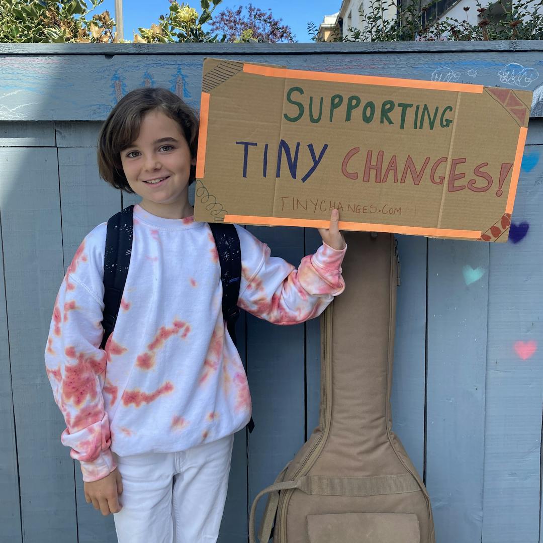 child holding handmade sign that says supporting tiny changes