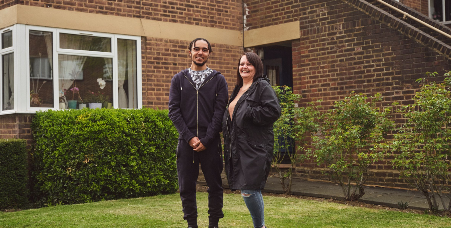 Two people smiling in front of a home
