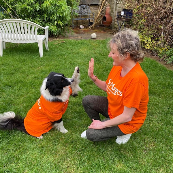 Image of a woman high fiving her dog, both in St Mungo's t-shirt