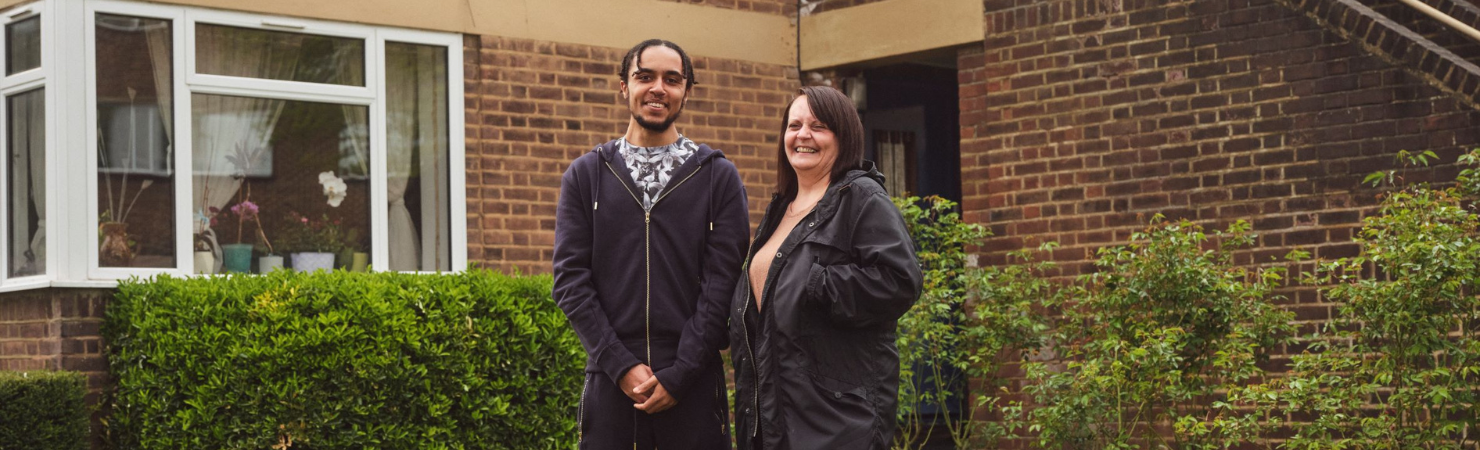 Two people smiling in front of a home