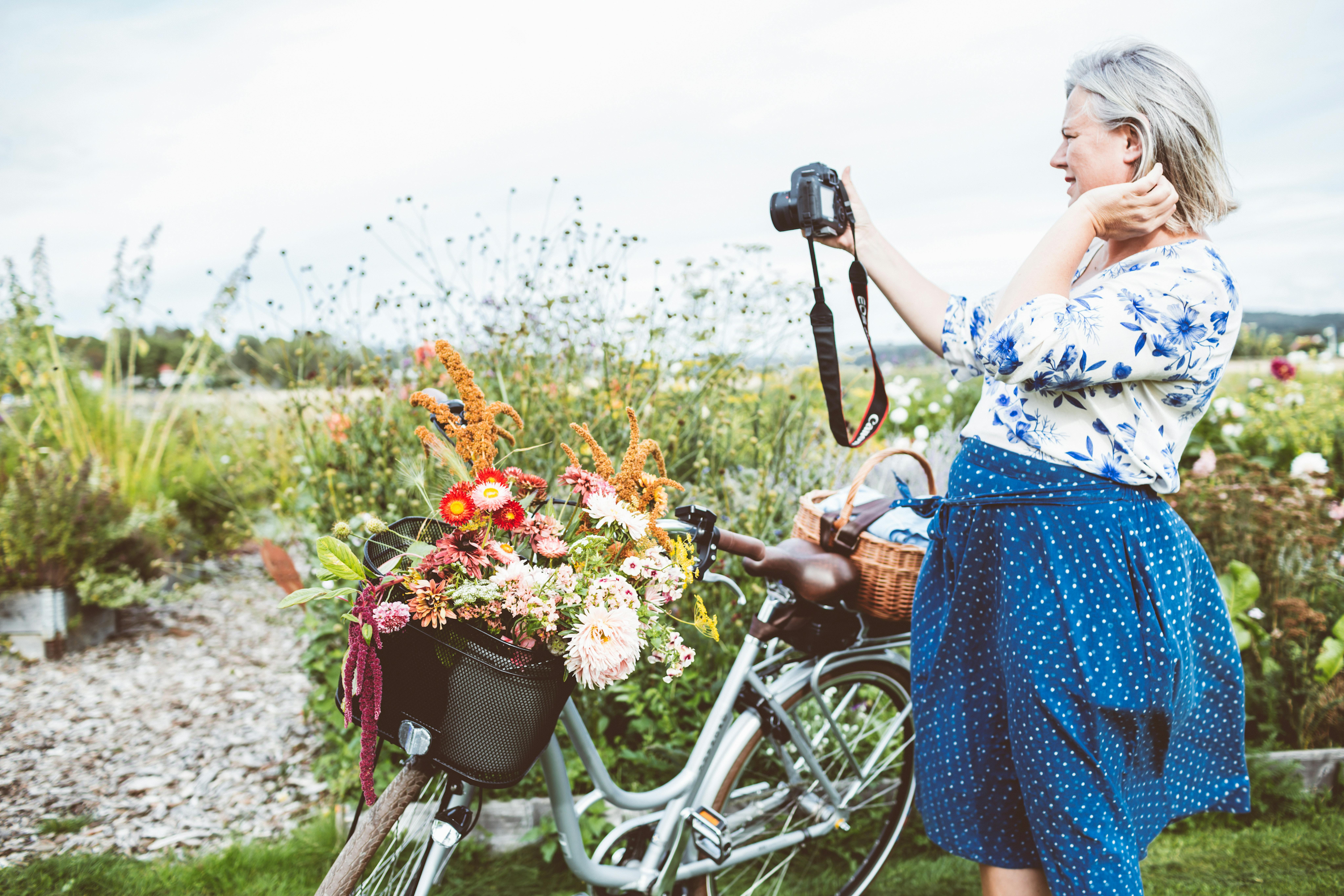 Kvinna jämte en cykel fotograferar blommor. 