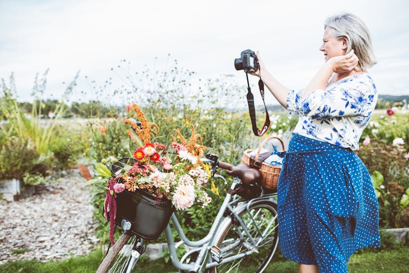 Kvinna jämte en cykel fotograferar blommor.