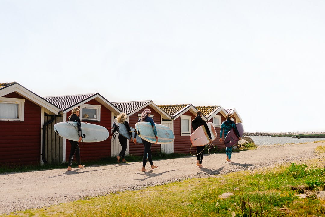 Ett kompisgäng går med surfbrädorna under armen påväg ner mot havet.