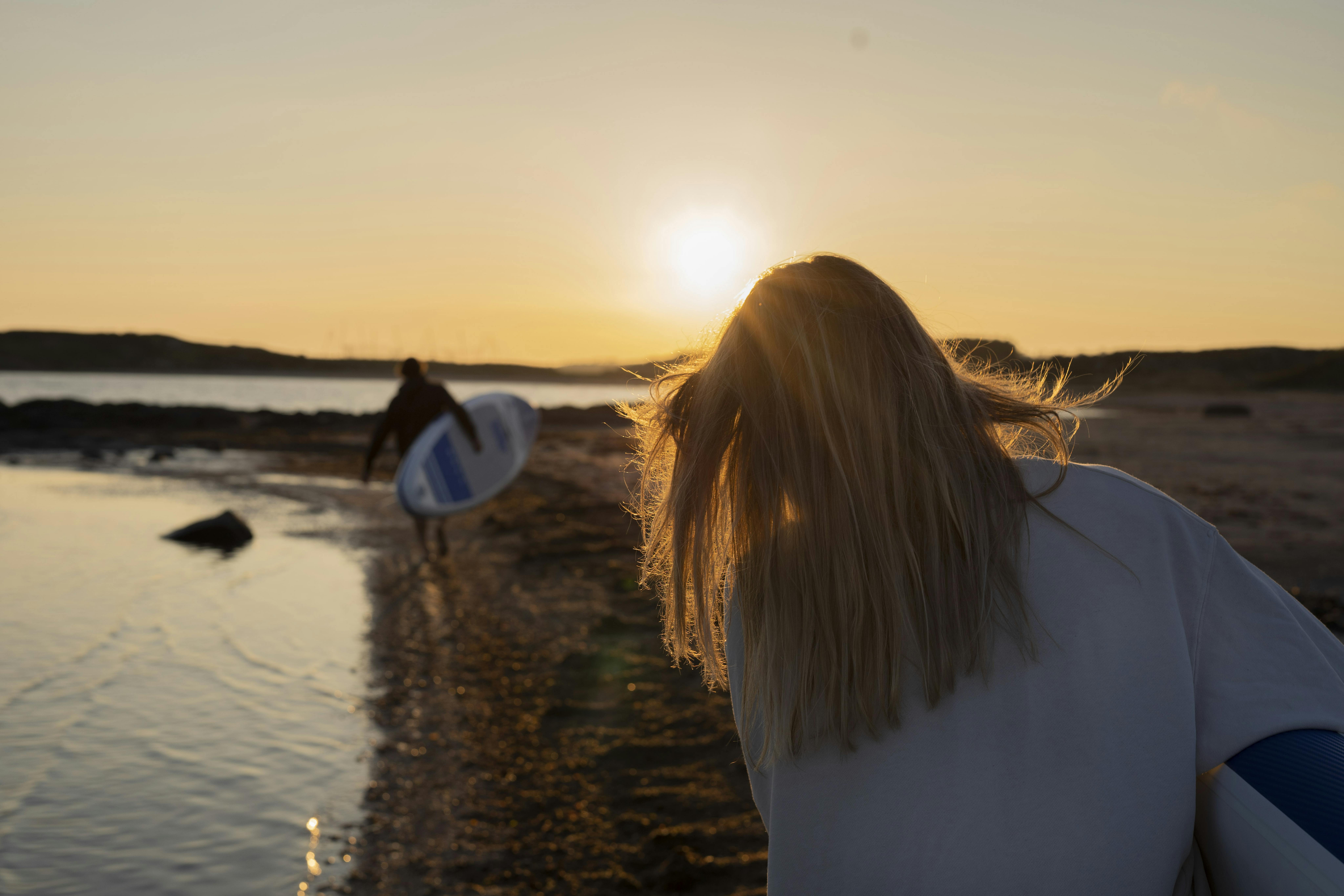 Mann und Frau tragen SUP Boards am Strand im Sonnenuntergang.