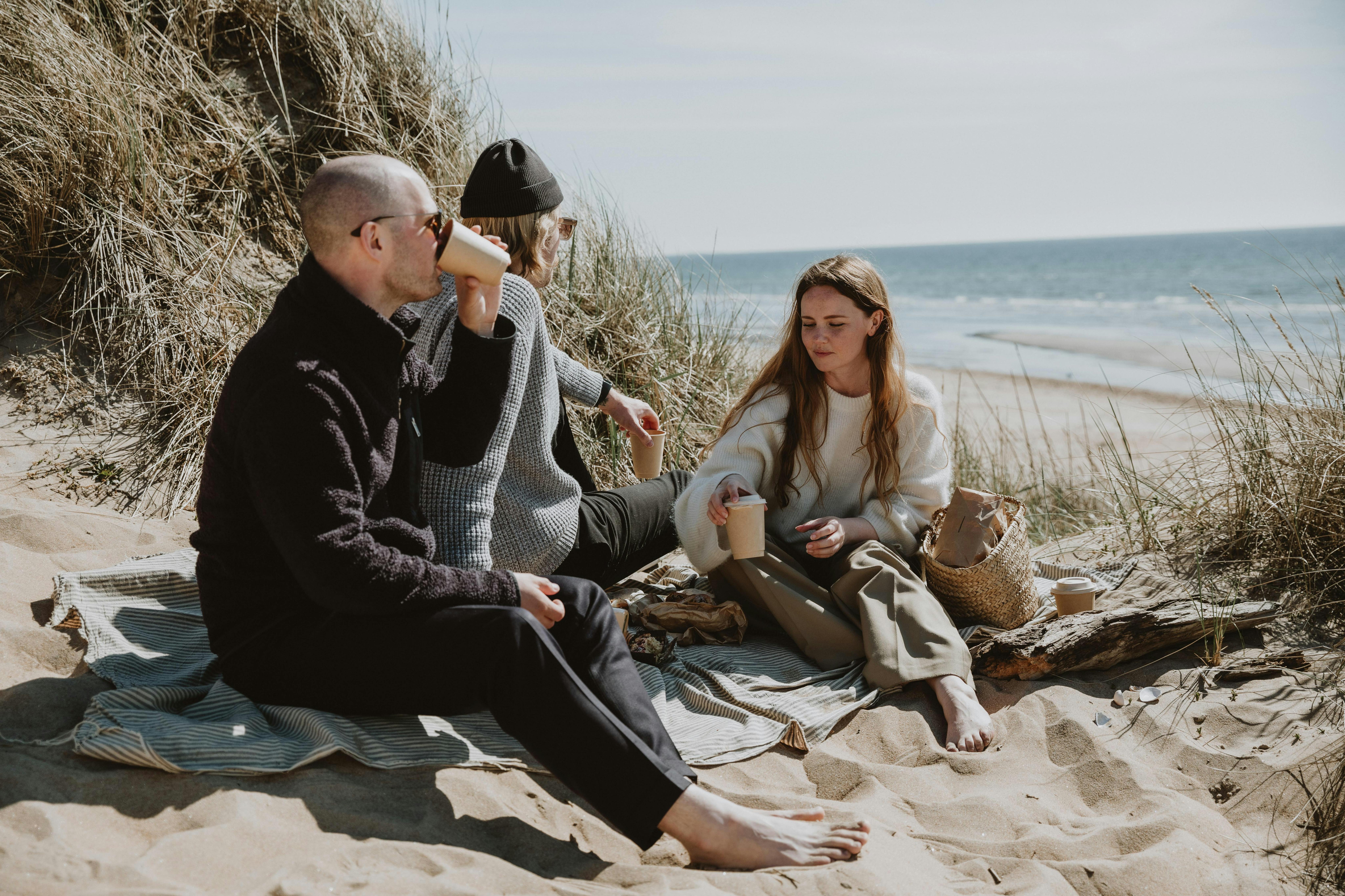 Drei Personen beim Picknick in den Dünen mit Blick aufs Meer.