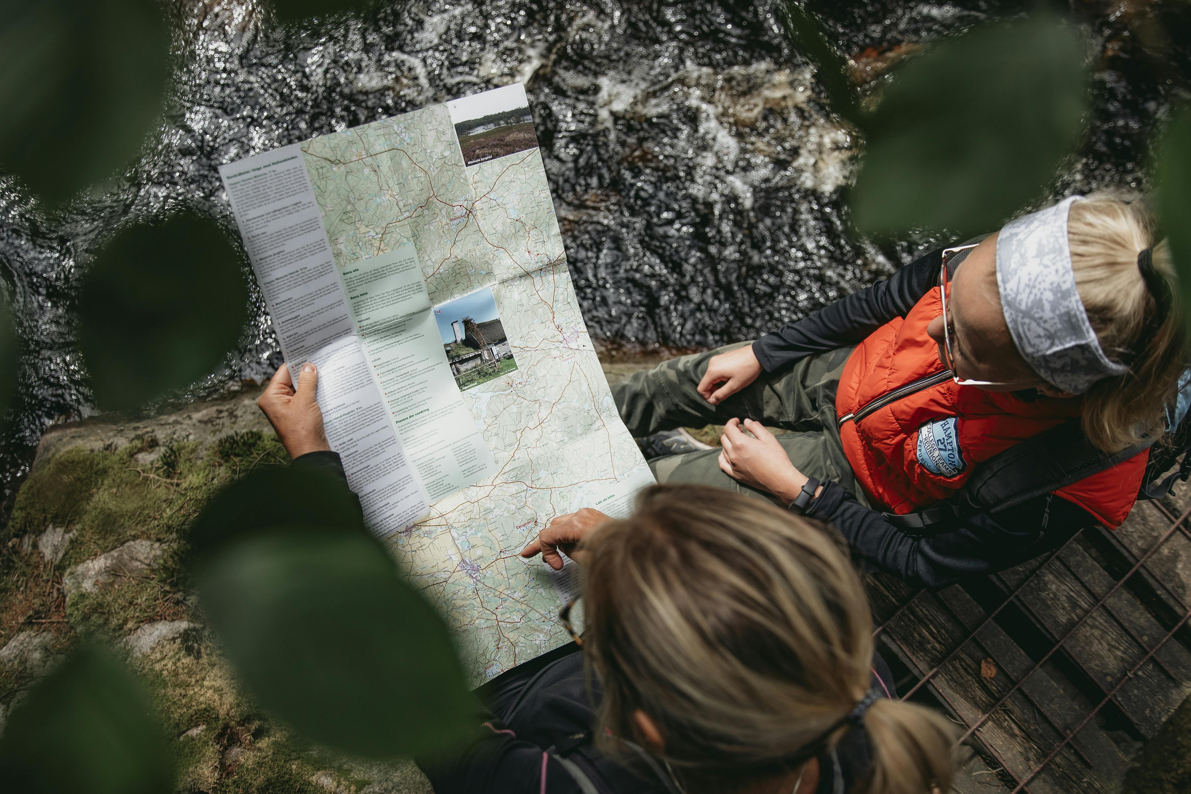 Två personer sitter i skogen och kollar på en karta över Hallandsleden.