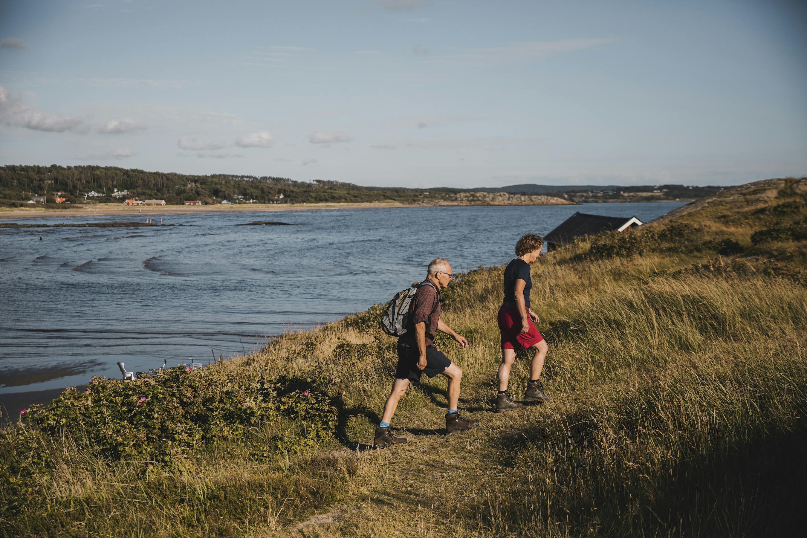 Två personer promenerar upp för en slänt med utsikt över havet.