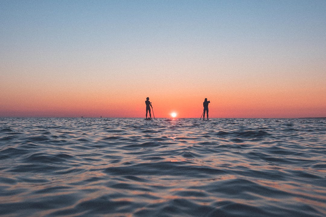Två personer paddlar ut mot solnedgången.