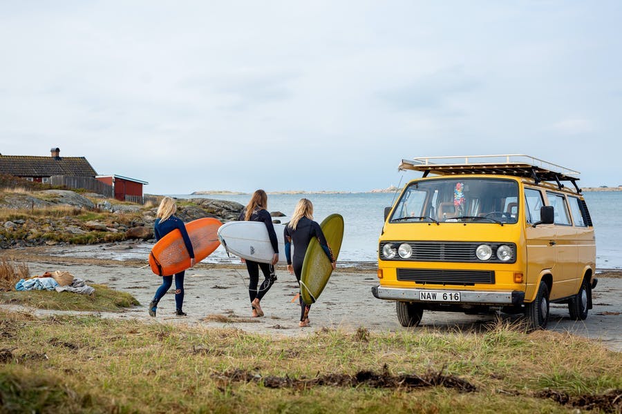 Kompisgäng går förbi surfbussen med surfbrädorna under armen.