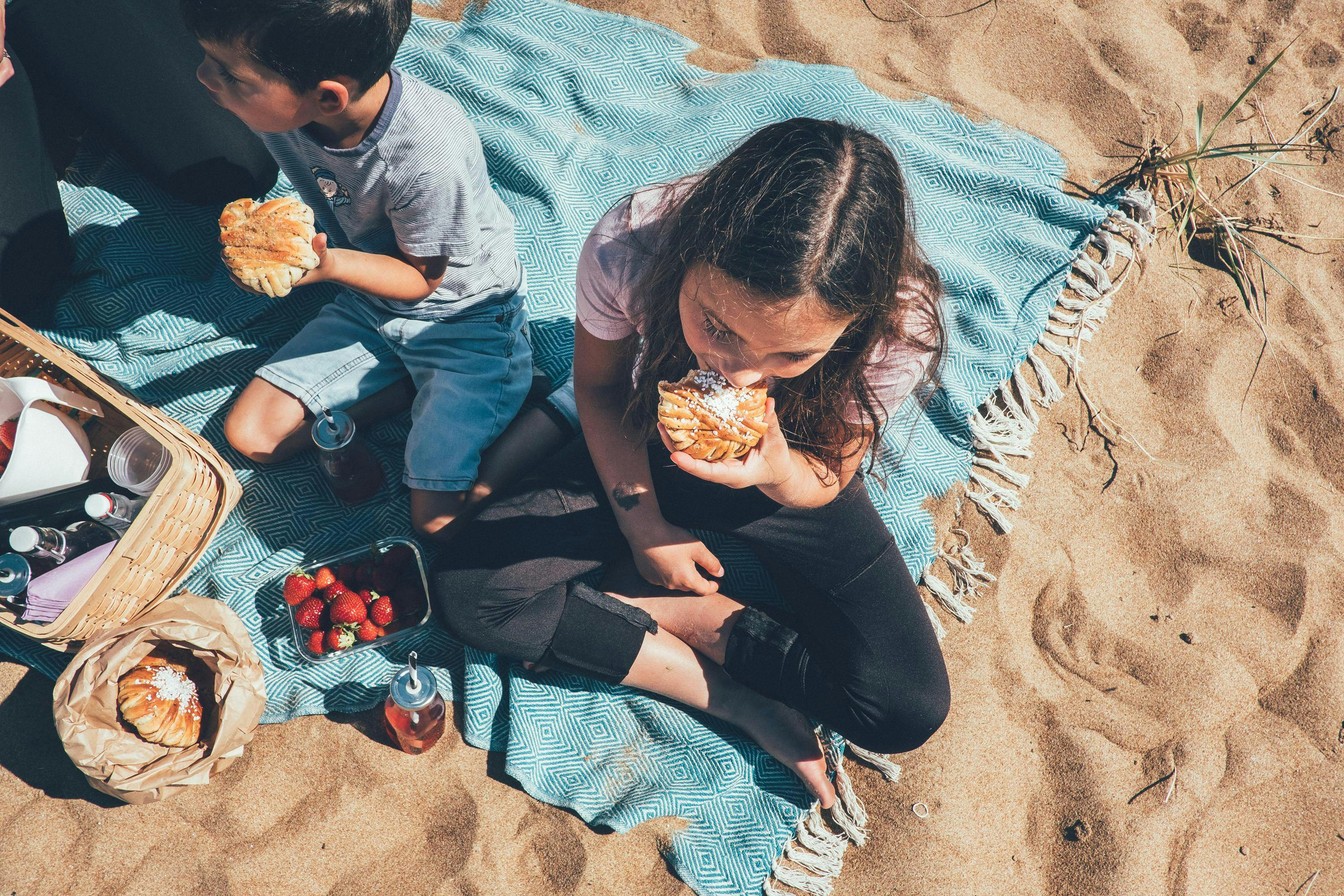 Två barn äter varsin bulle på stranden.