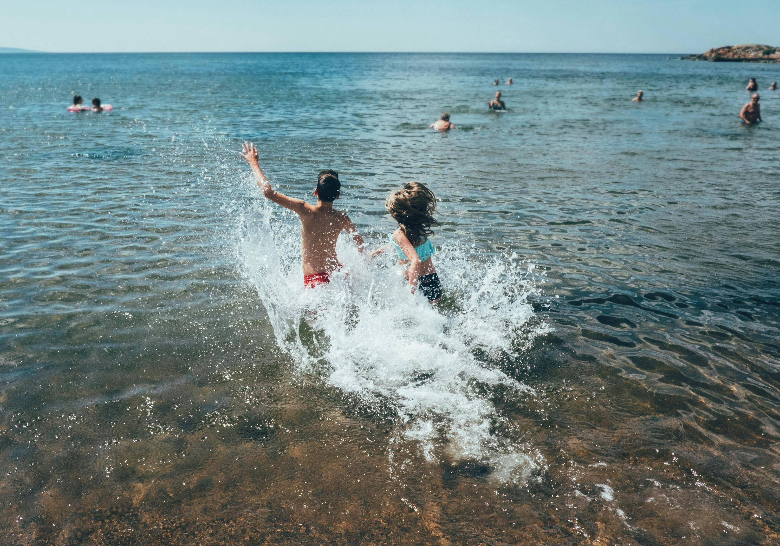 Två barn springer ut i havet så att vattnet skvätter.
