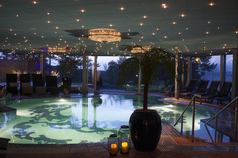Skymningsbild innifrån Säröhus inomhuspool med kristallampor i taket och upplyst pool.