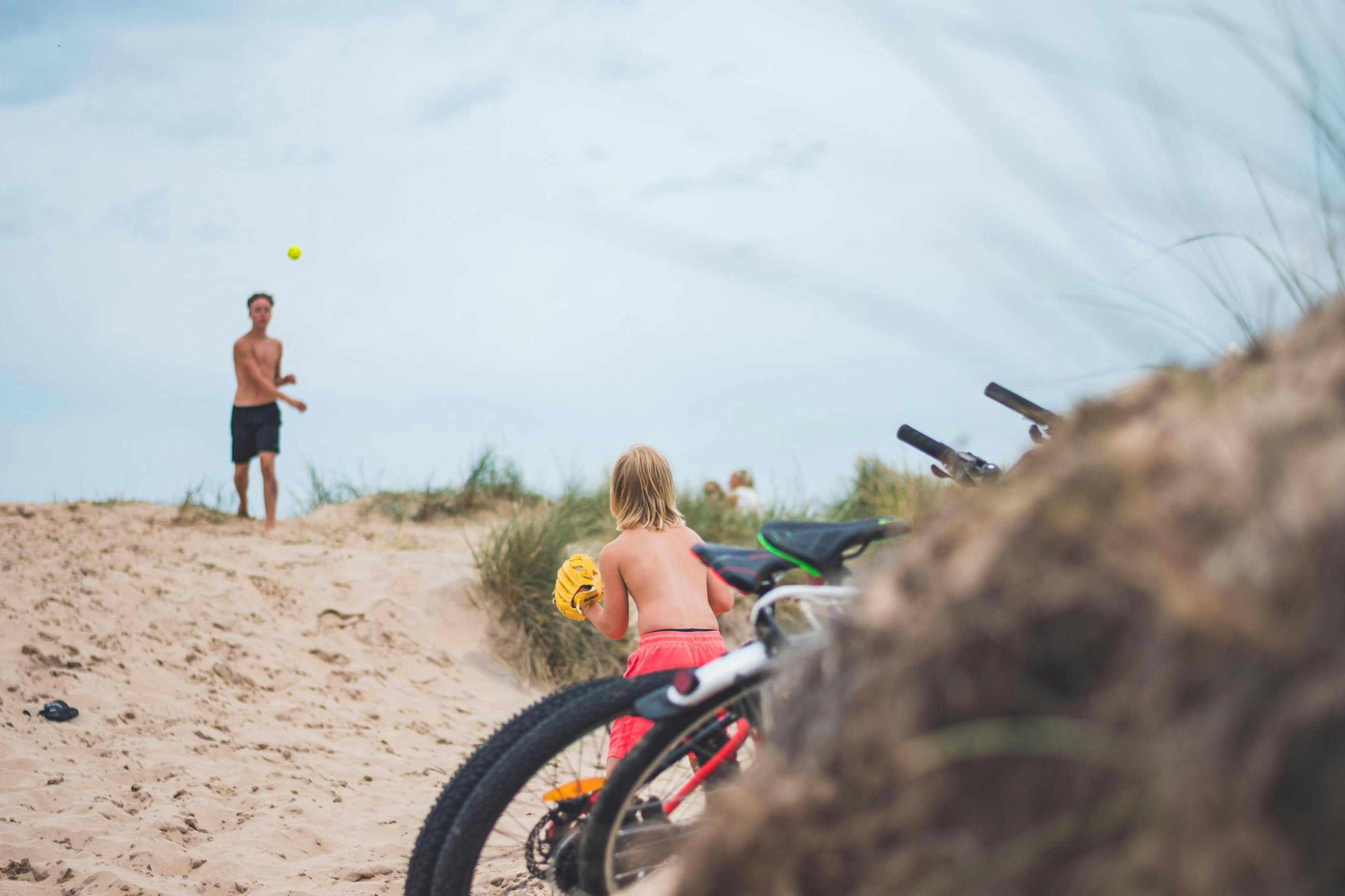 Två barn kastar boll till varandra på stranden.