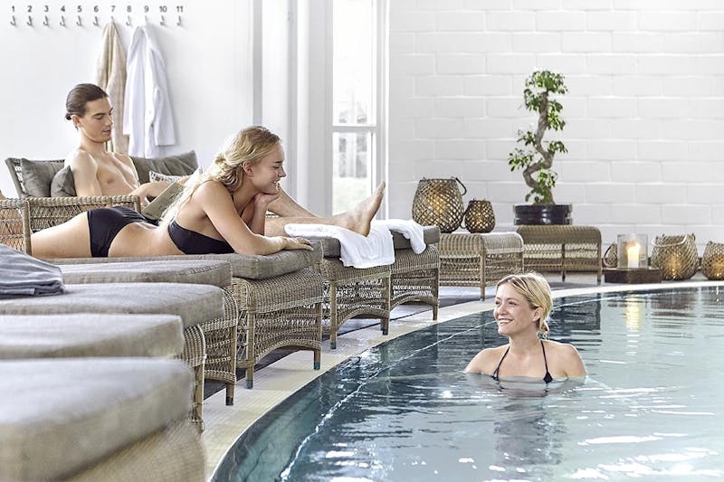 Två personer sitter i varsin fåtölj vid poolkanten och en person befinner sig i polen.