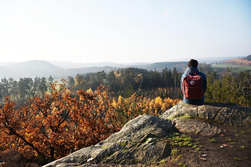 En person med ryggsäck sitter på klippan och tittar ut över skogarna.