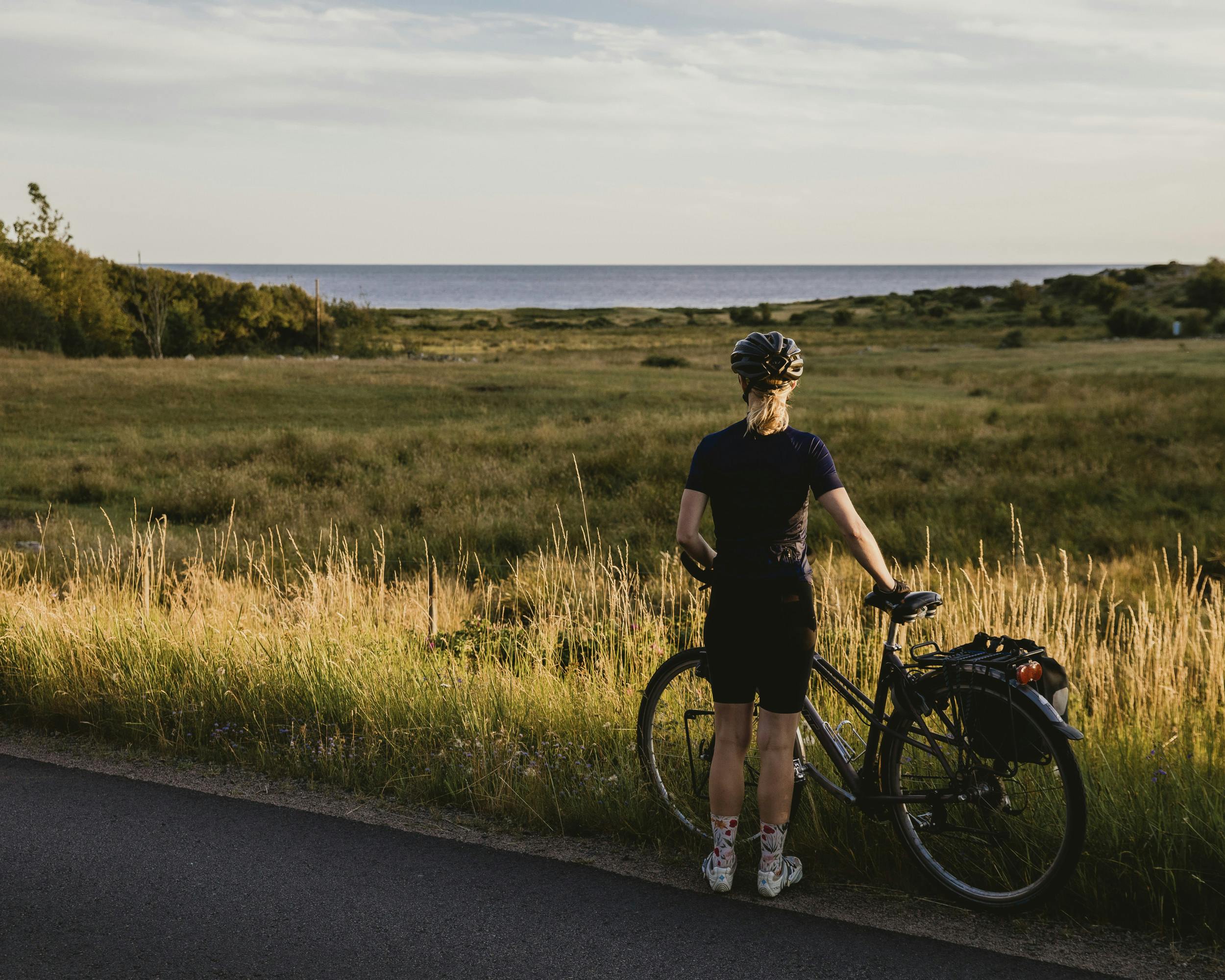 Frau steht mit Rad am Straßenrand und blickt aufs Meer.