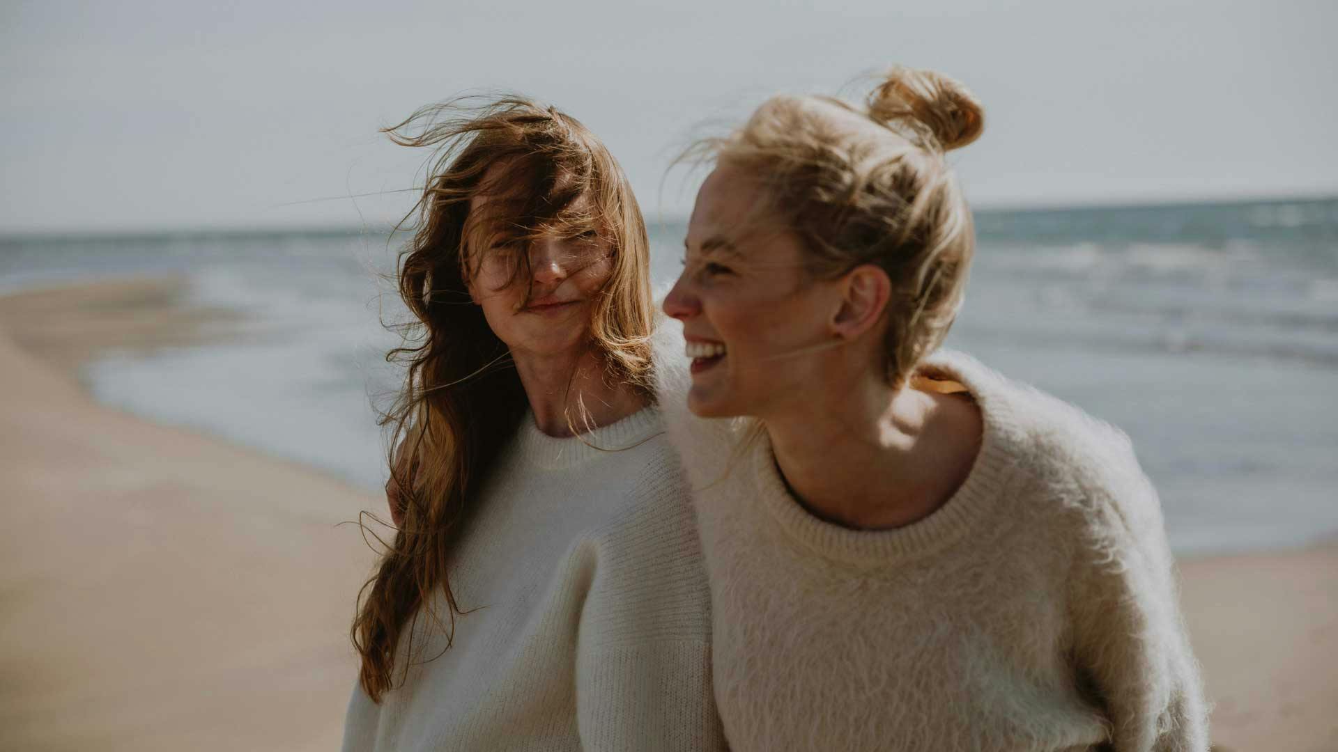 Zwei fröhliche Freundinnen am Strand mit Meer im Hintergrund