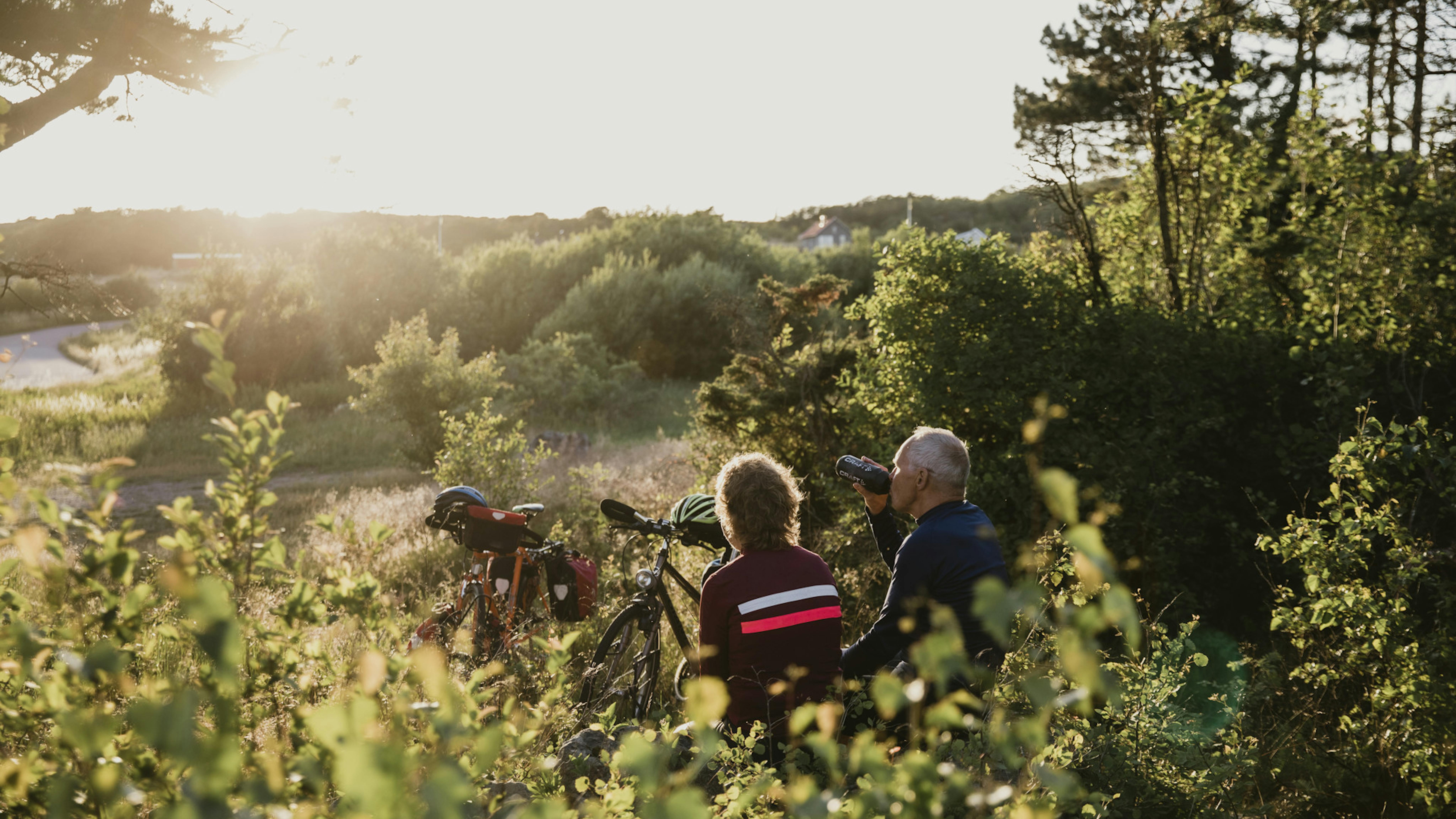 Två cyklister sitter och dricker vatten i en skogsdunge