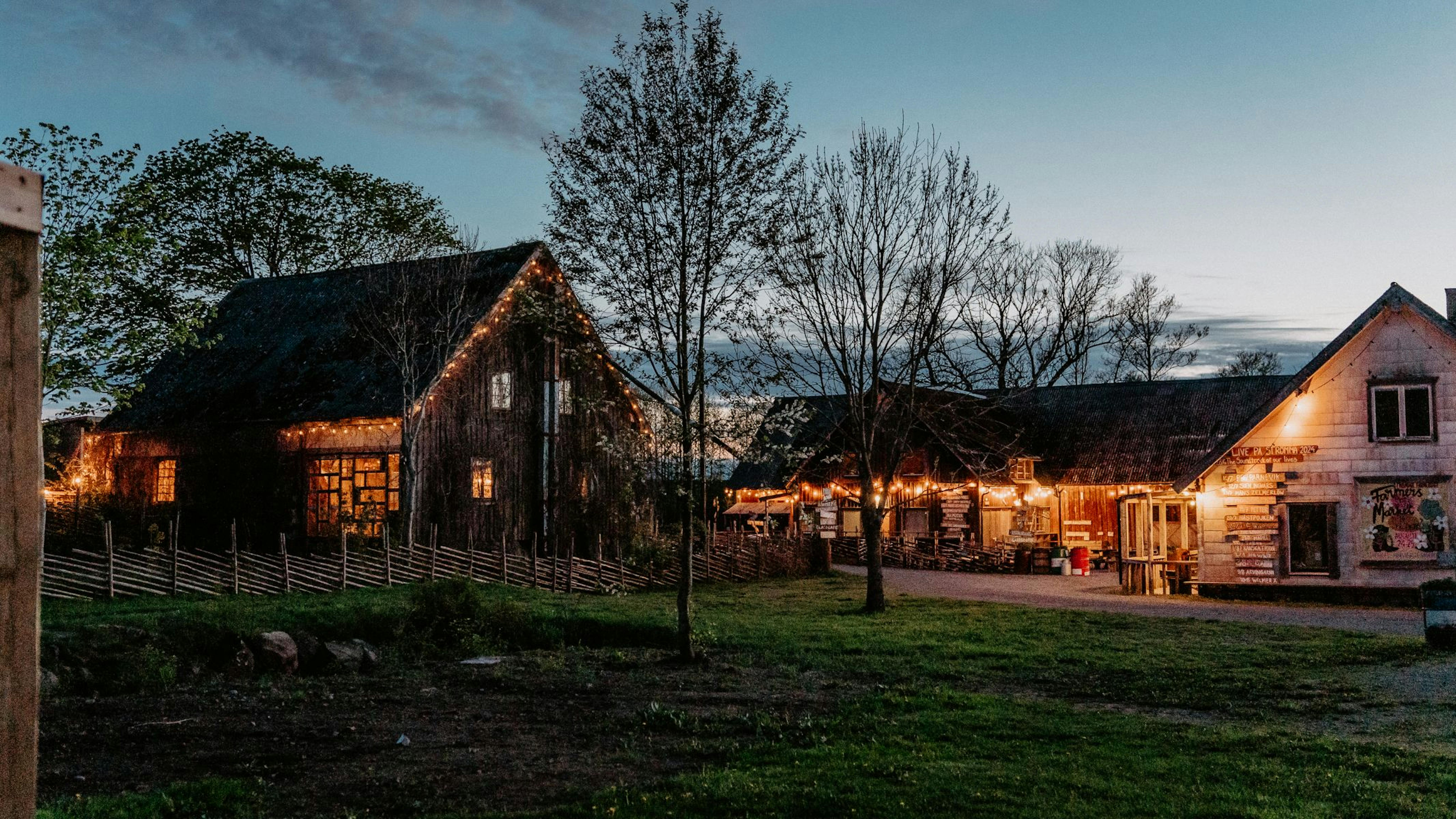 Bild på Strömma Farmlodge utemiljö, lador och hus upplysta på kvällen.