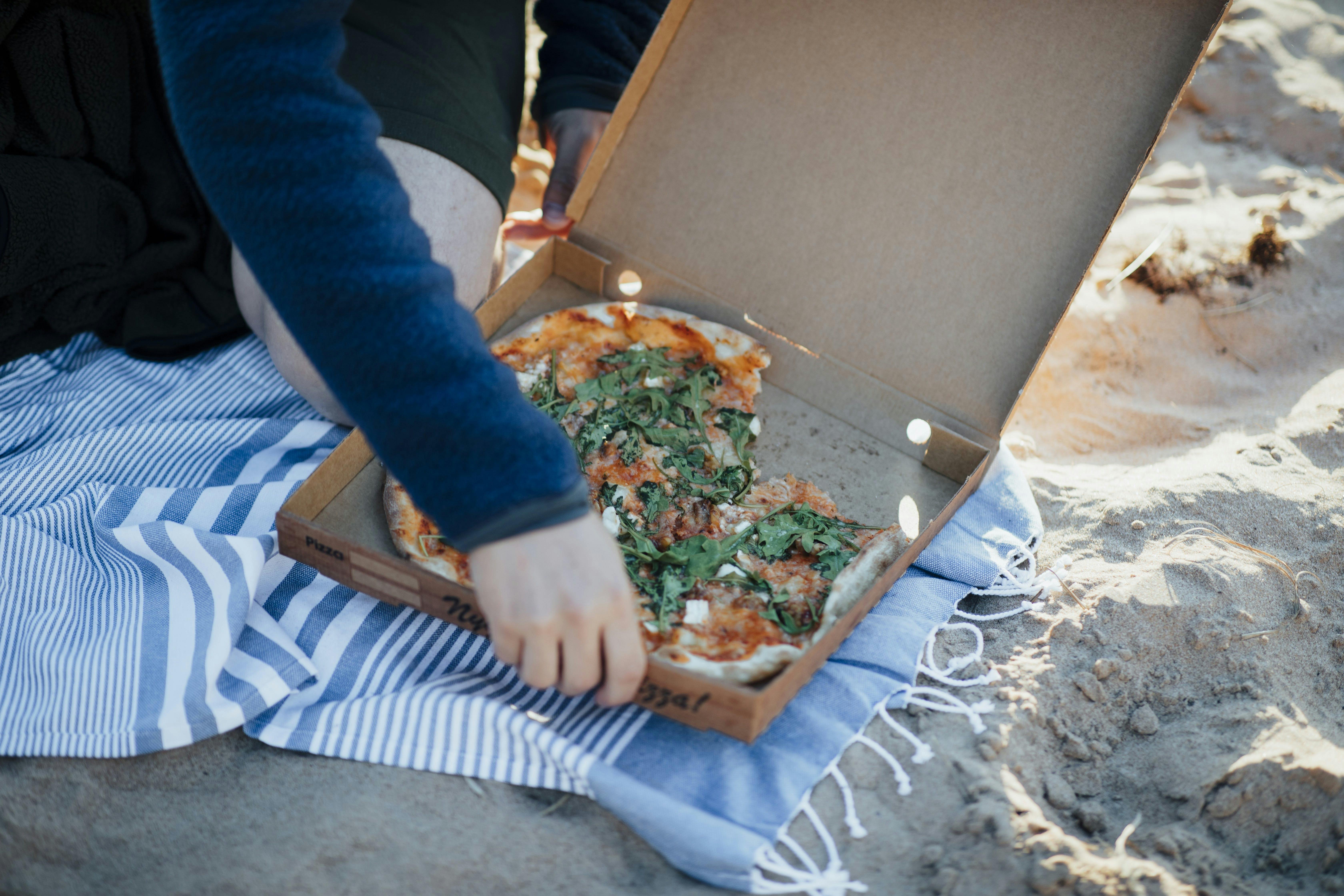 En person tar en bit pizza från stranden.