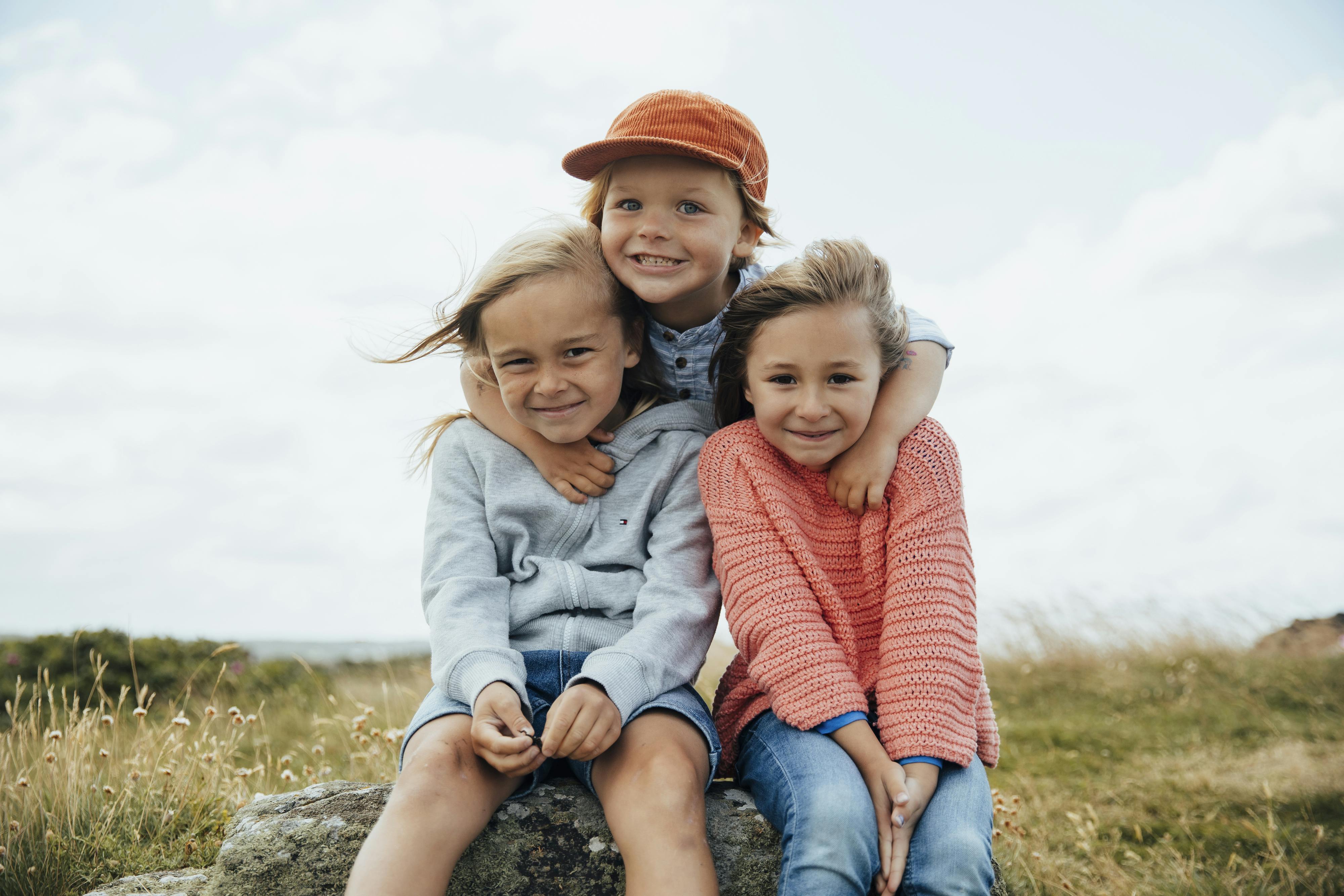 Drei Kinder sitzen auf einem Stein und grinsen in die Kamera.