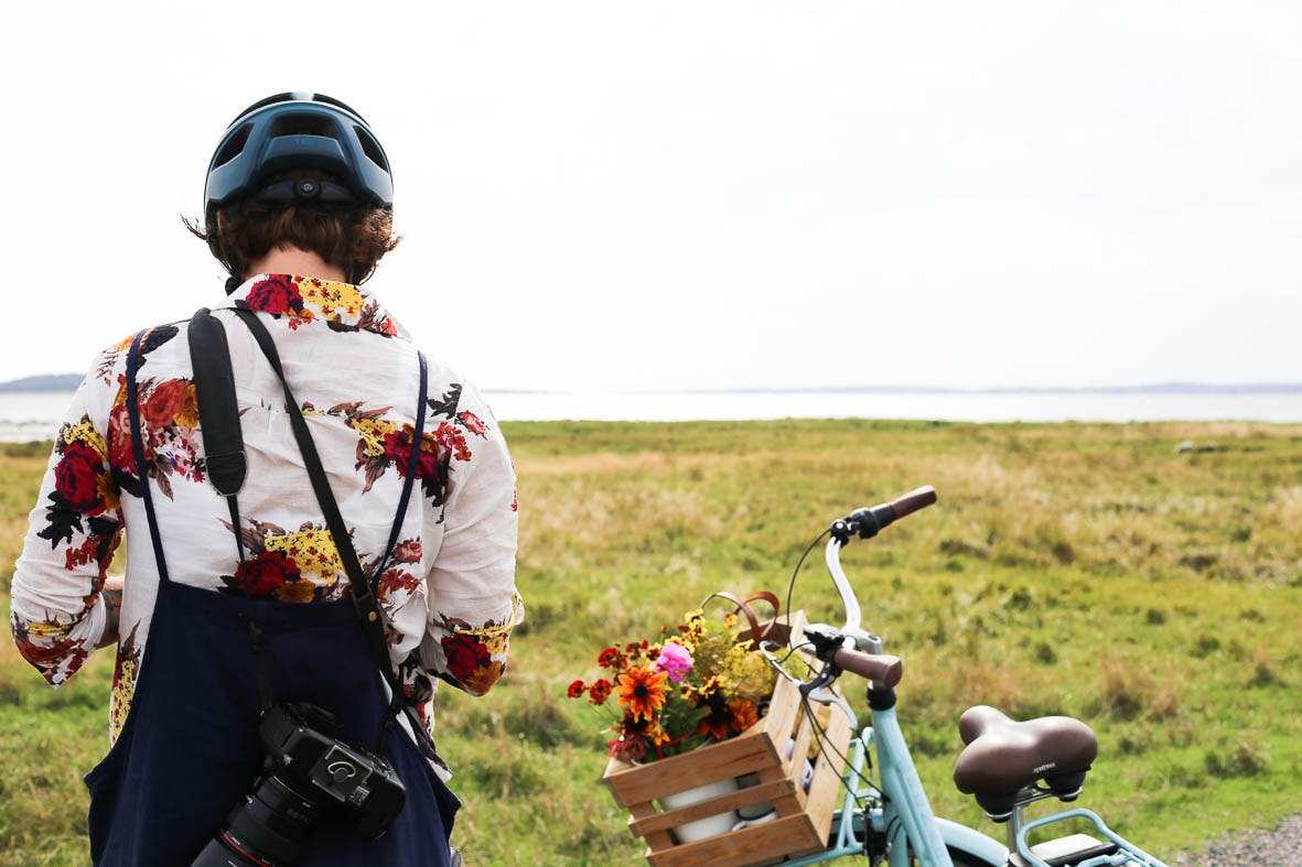 Kvinna med cykelhjälm och kamera står vid sin cykel