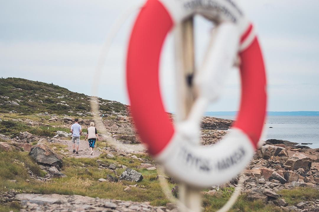 Två personer går på en stig. I förgrunden syns en rödvit livboj.