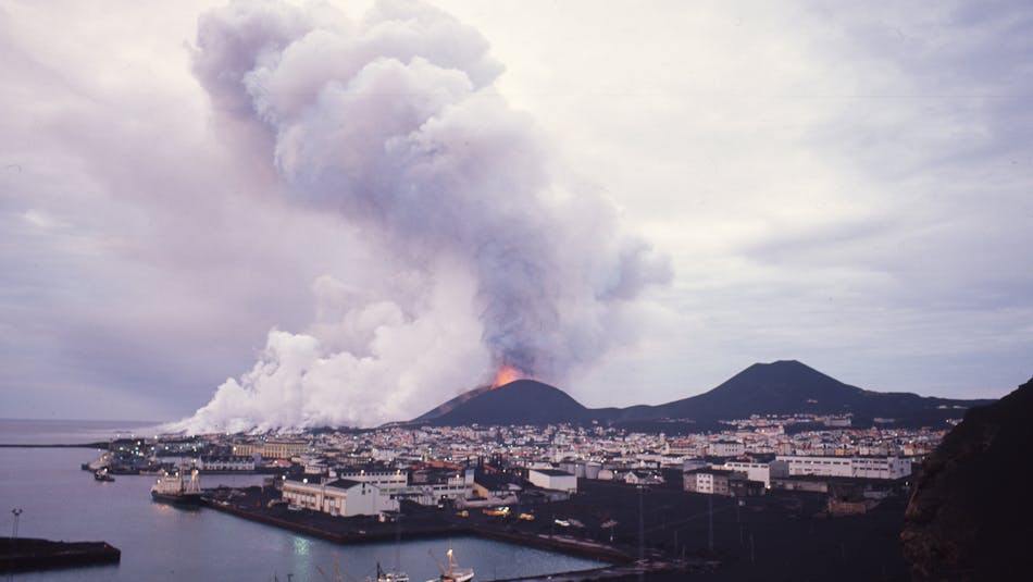 An erupting volcano spouting ash over a town on a small island