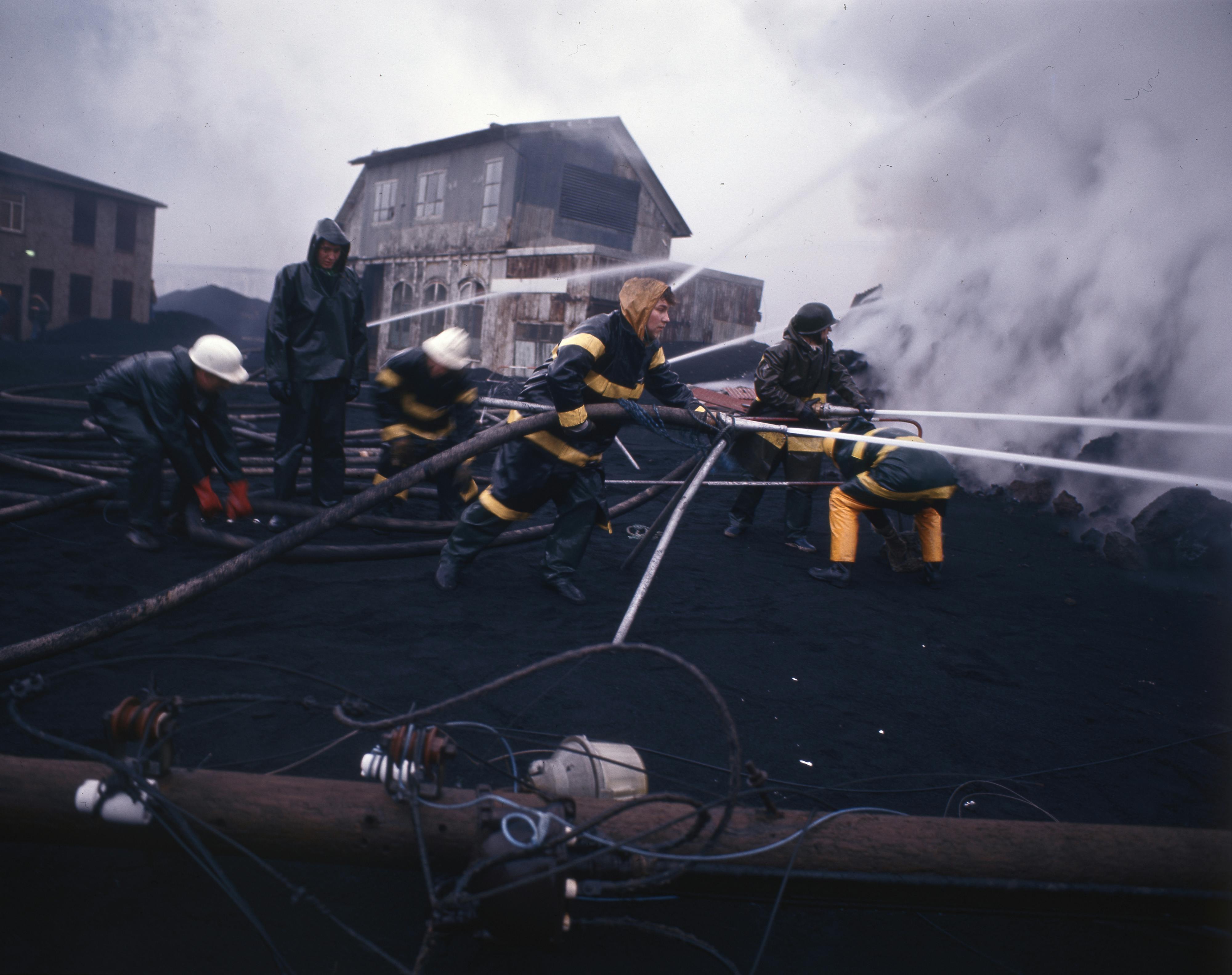 Firemen with water hoses combatting an active lava front.