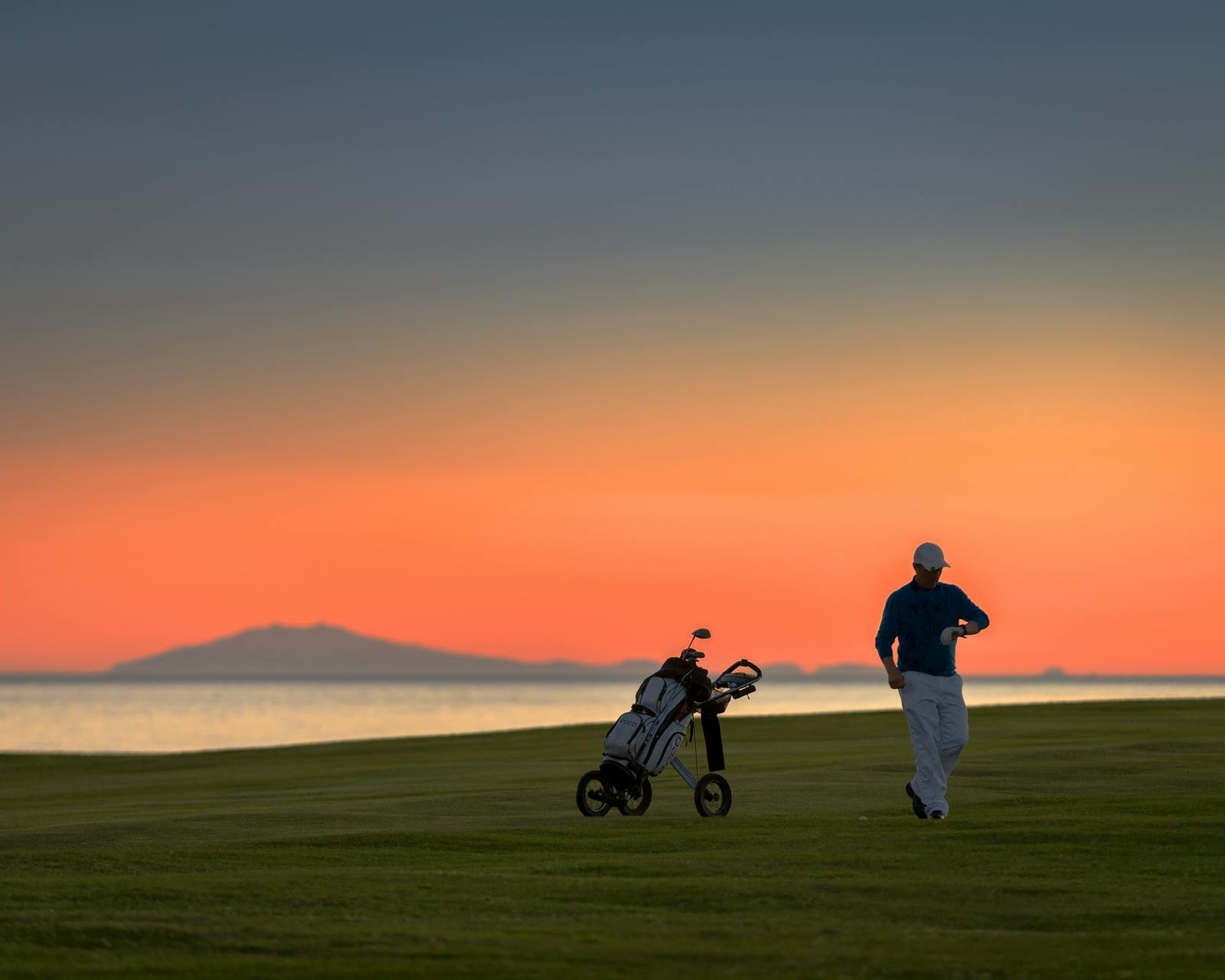 golfer looking at his watch, sunset lights the sky red
