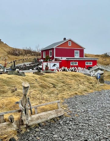 A red house with a garden full of whale bones and wood and rock sculptures