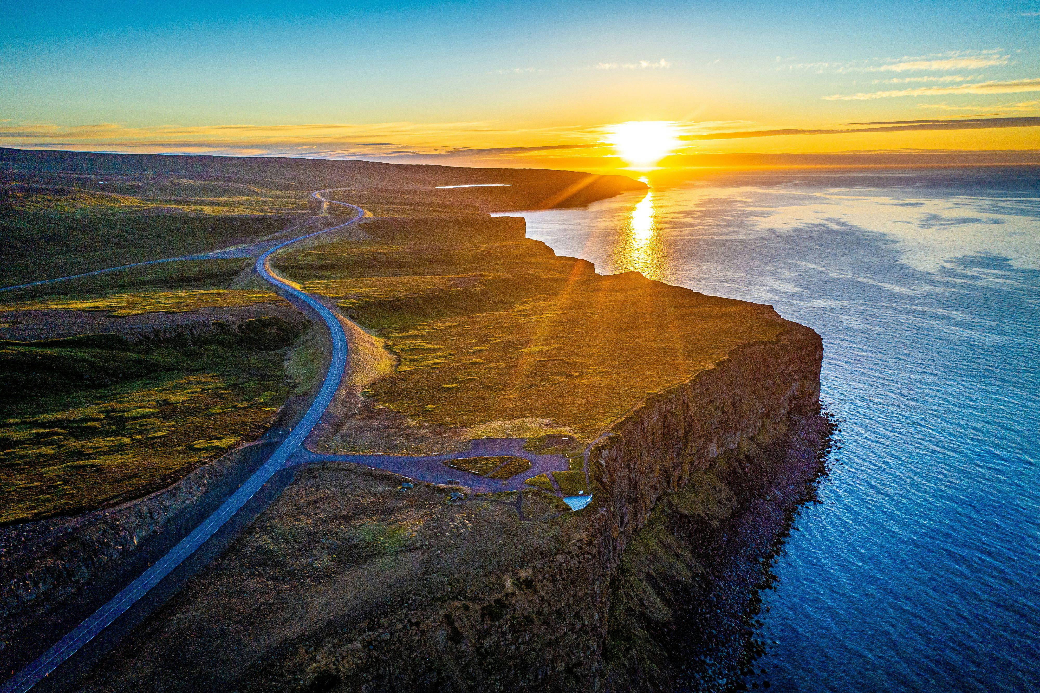 Midnight sun setting along the Arctic Coast Way, a road, cliffs and ocean in the picture