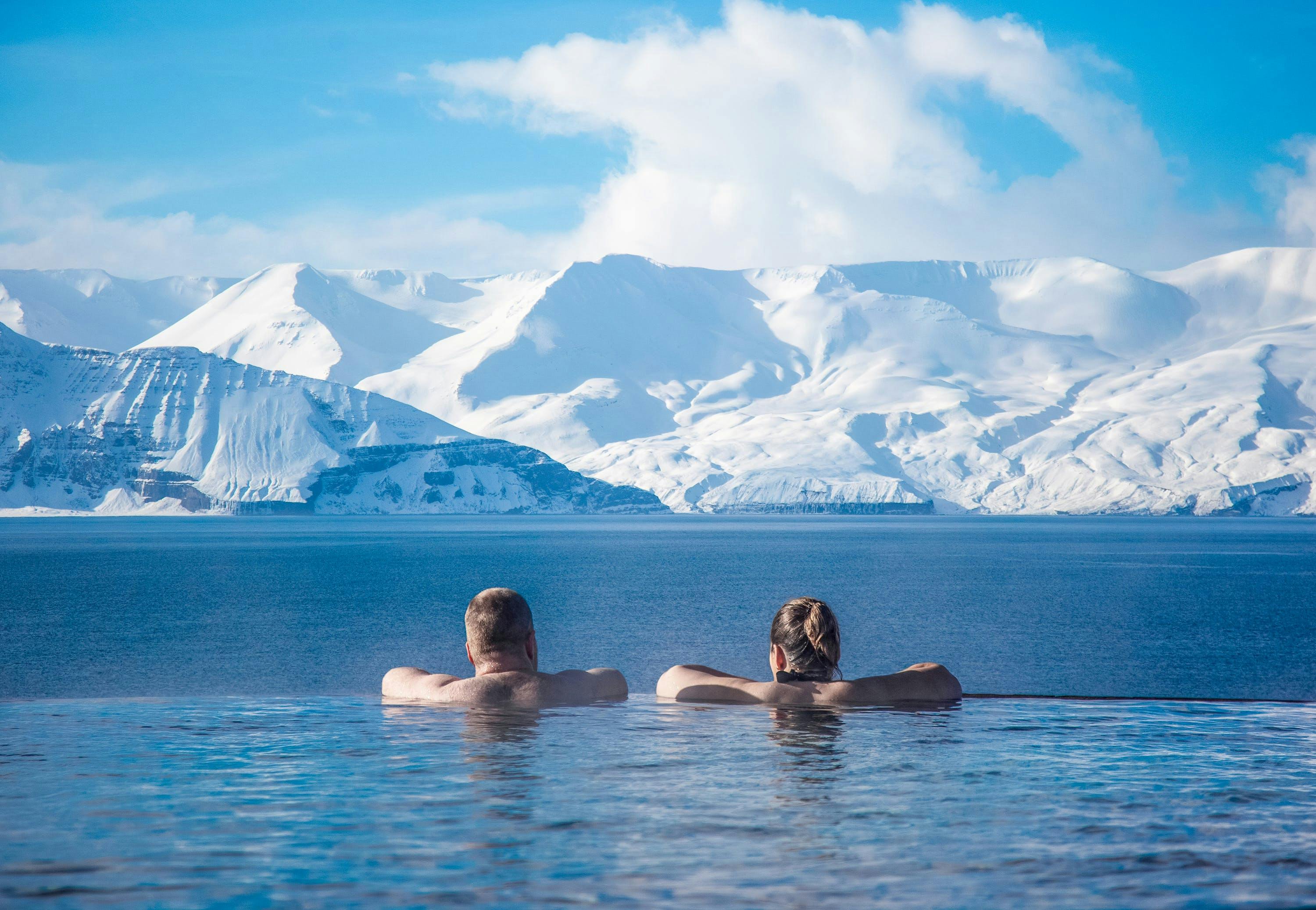 A couple beople bathing and facing snowy mountains