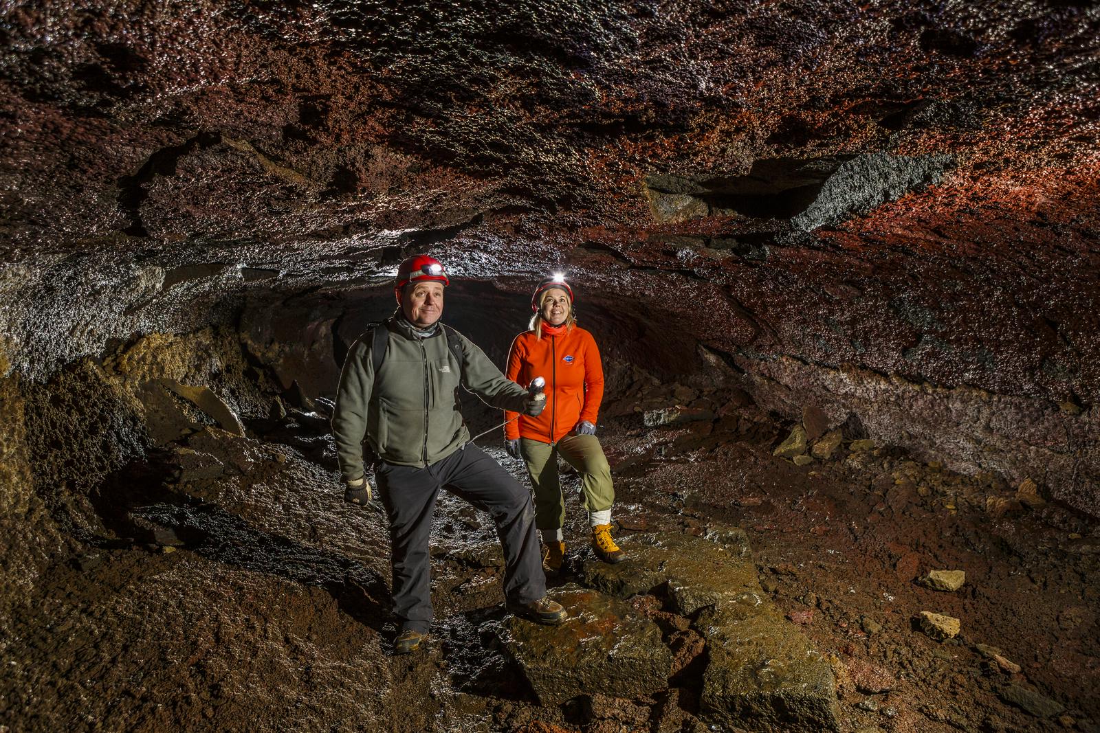 Two people wearing helmets and headlamps standing inside a cave