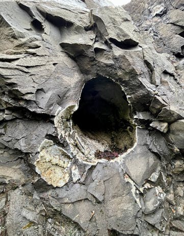 A large hole in a grey cliff with mineral coating on the inside