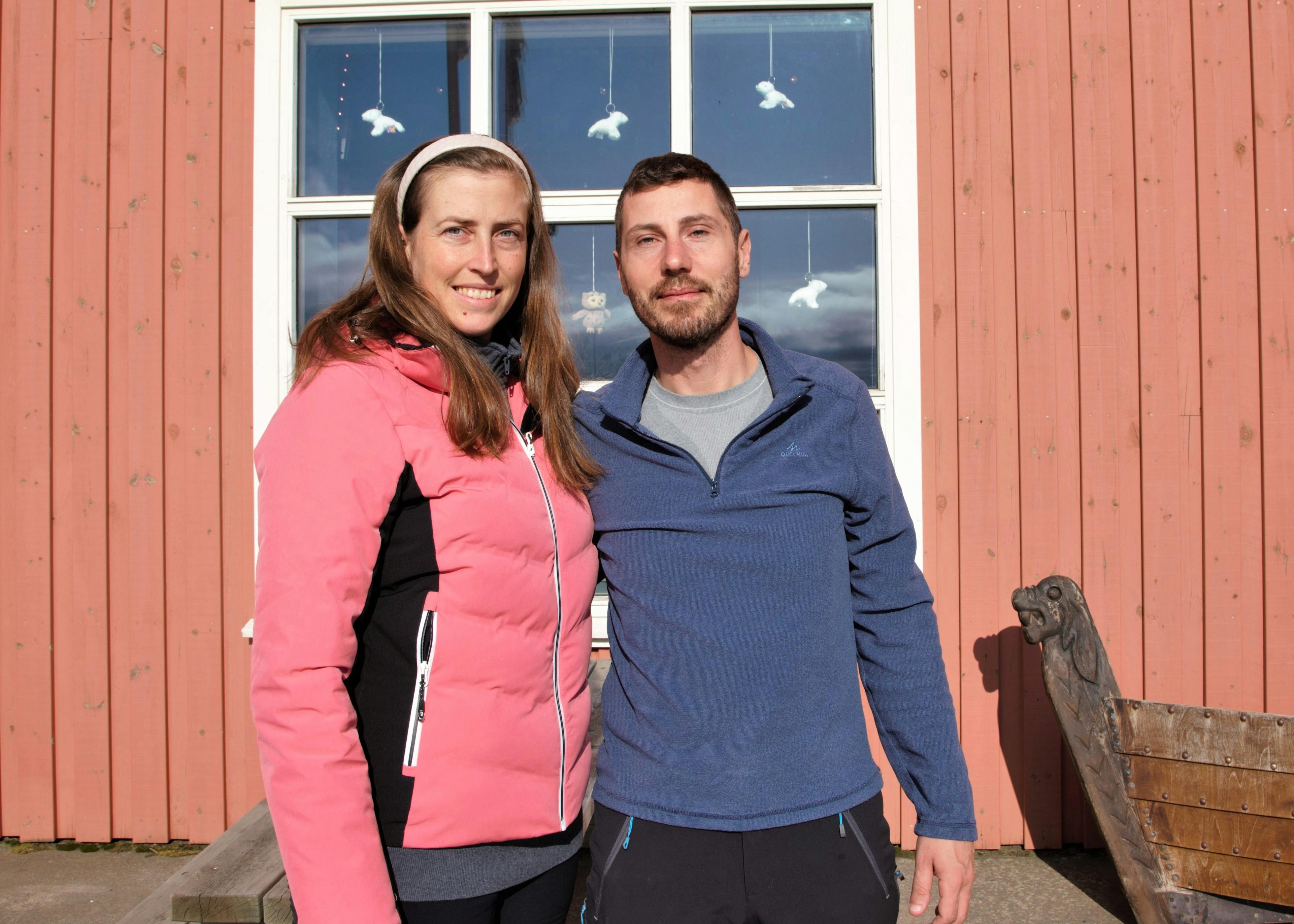 Young woman and man standing in front of a red timber house, the sun is shining