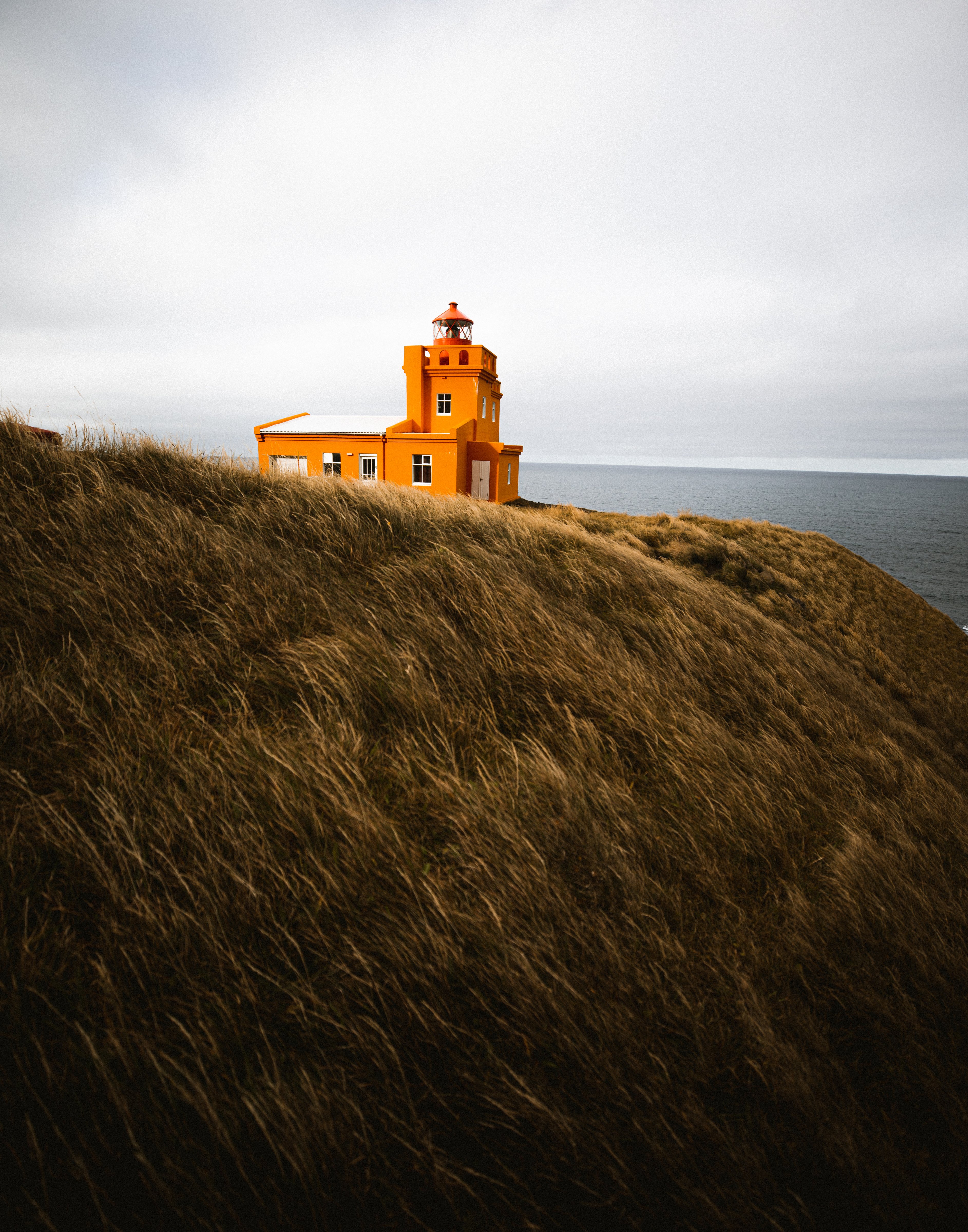 The orange Sauðanes lighthouse standing on a cliff surrounded by grass on Tröllaskagi peninsula in North Iceland