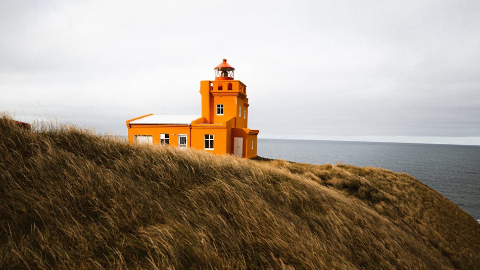 The orange Sauðanes lighthouse standing on a cliff surrounded by grass on Tröllaskagi peninsula in North Iceland
