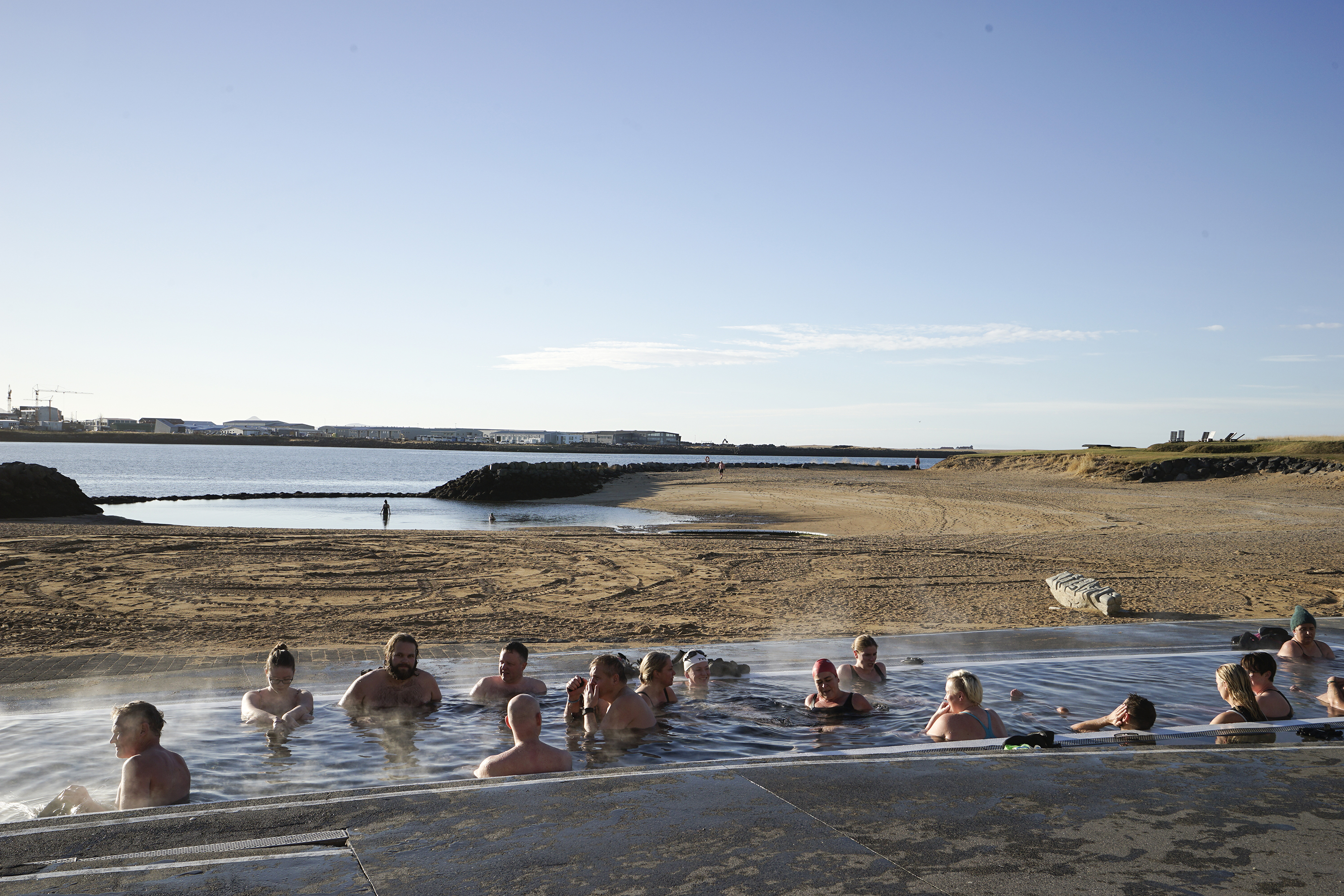 People relaxing in the geothermal pool at Nauthólsvík Geothermal Beach in Reykjavík, with the shoreline and ocean beyond.