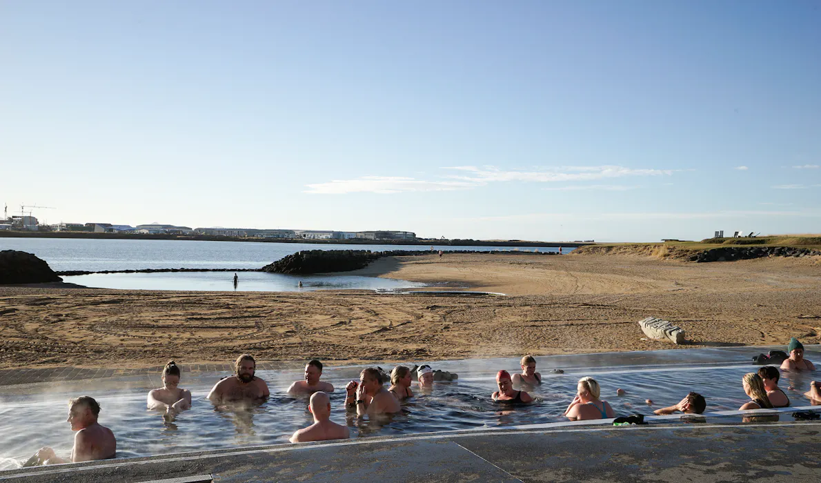 People relaxing in the geothermal pool at Nauthólsvík Geothermal Beach in Reykjavík, with the shoreline and ocean beyond.