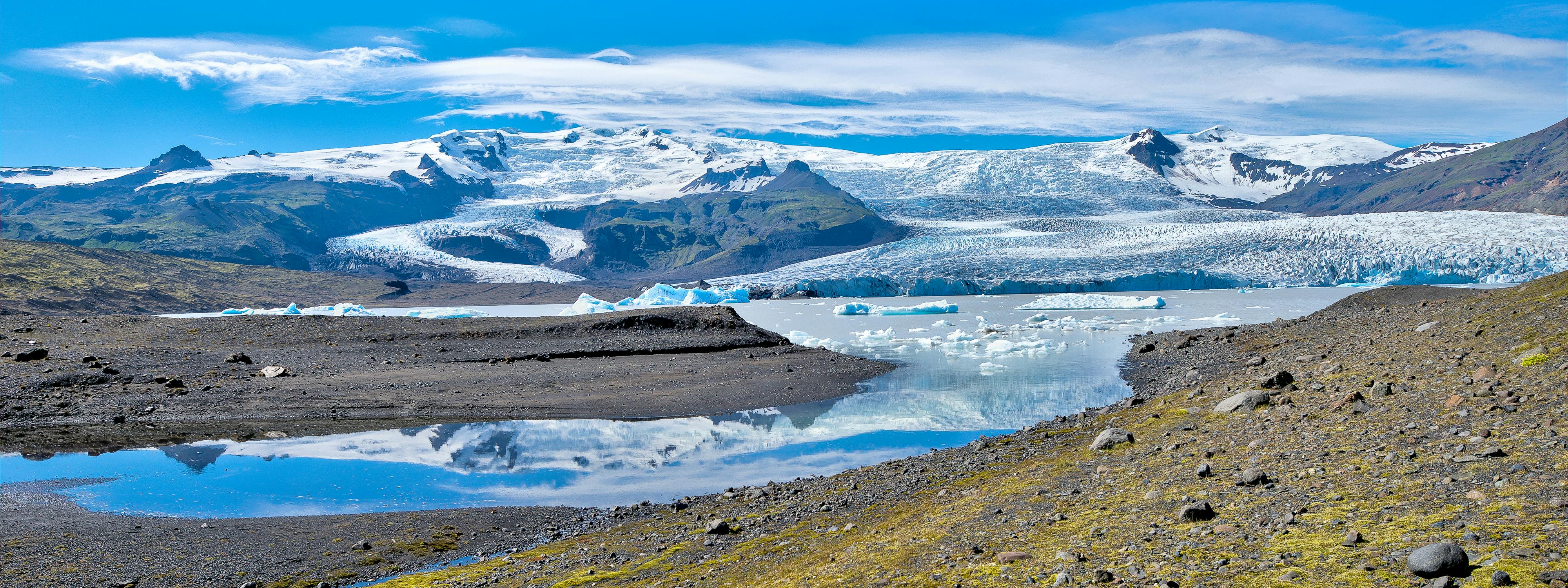 A glacier lake with icebergs in front of a river of ice flowing from an ice-covered volcano
