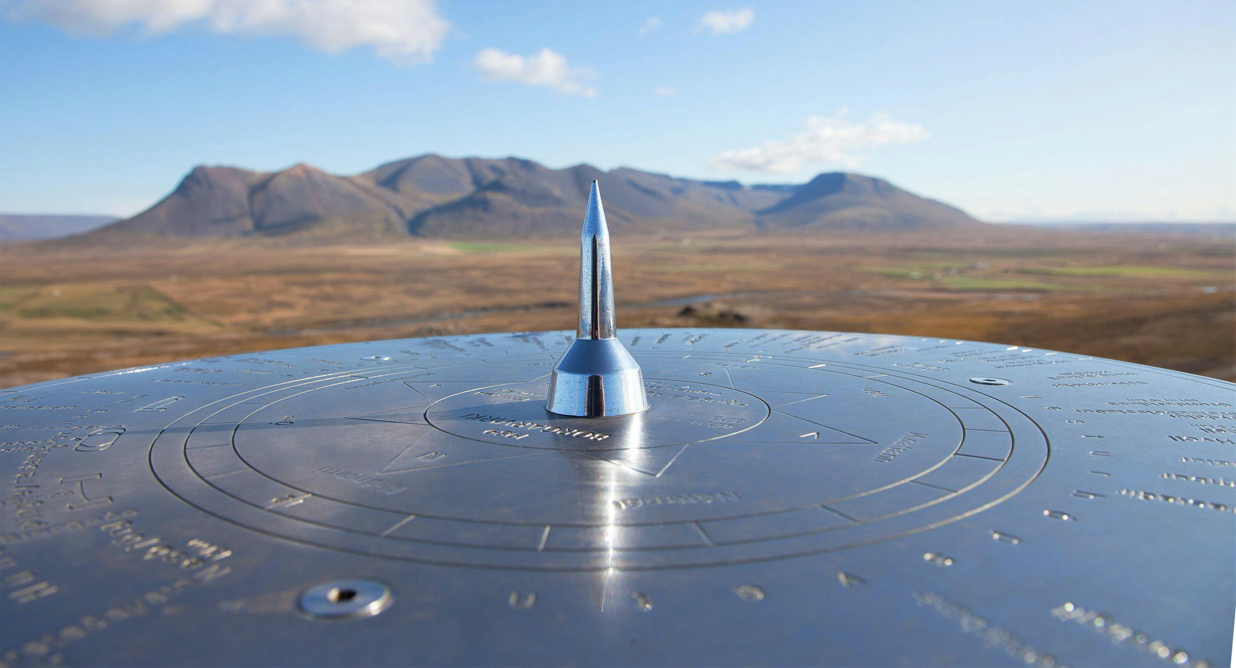 Closeup of a compass at Borgarvirki in the foreground, mountain group in the background