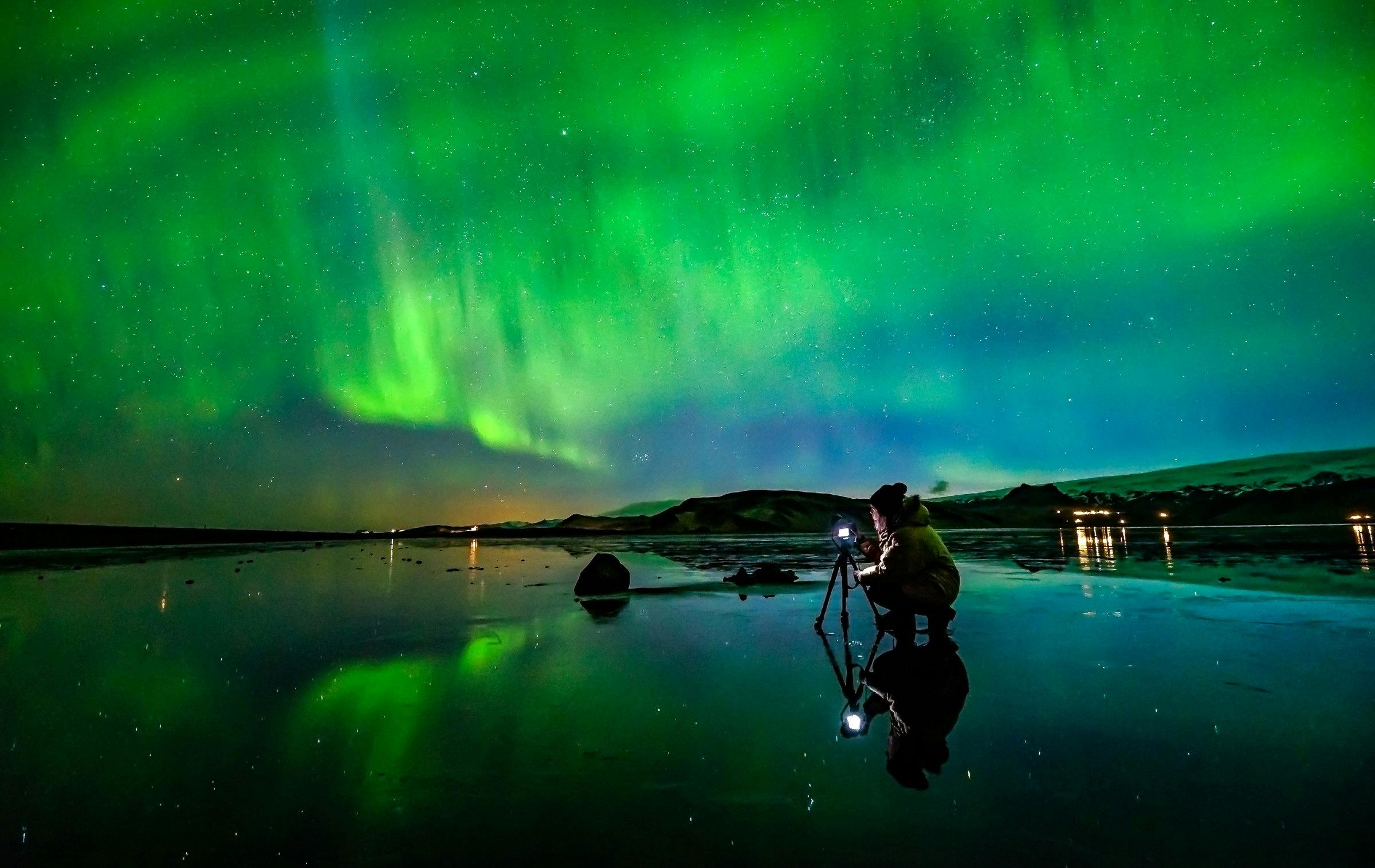 Woman taking photos of the northern lights at Dyrholaey sea cliffs 