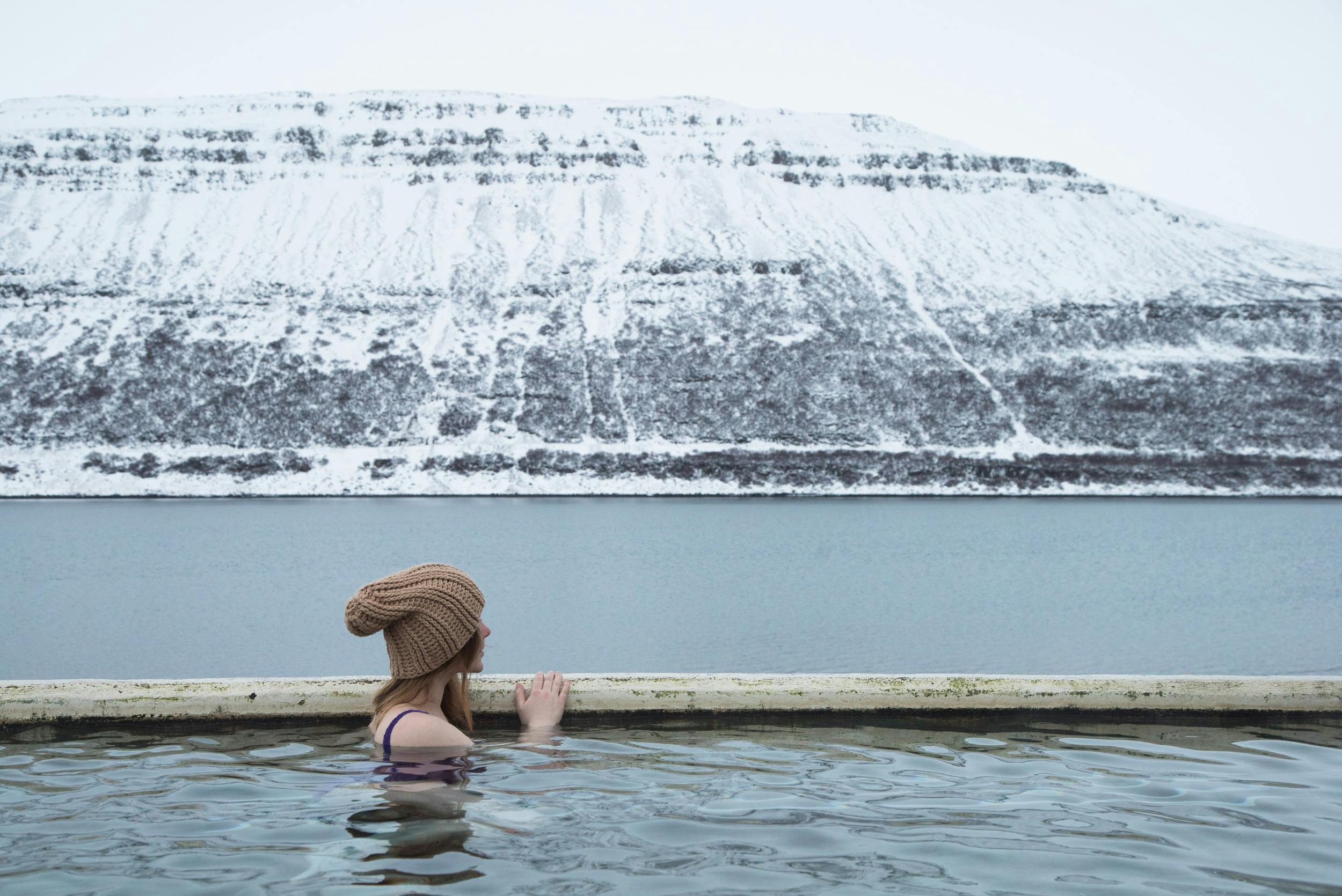Woman in Horgshlidarlaug swimming pool overlooking the sea and snowy mountain