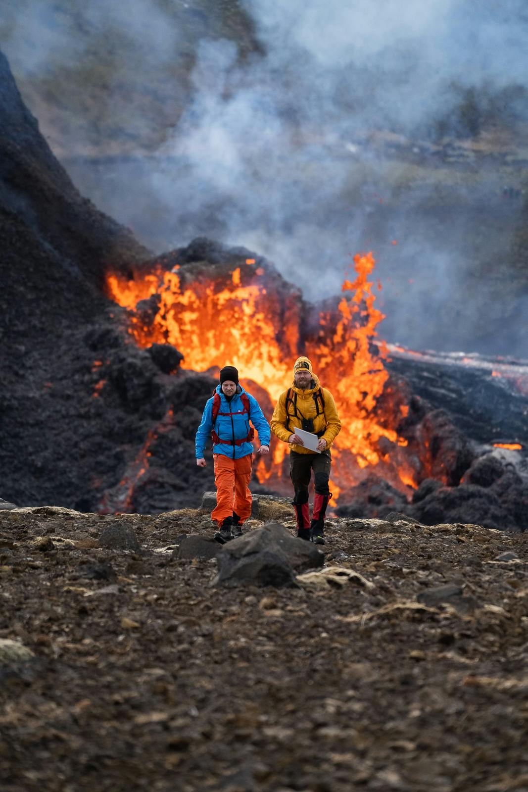 Two men walking past an erupting volcano