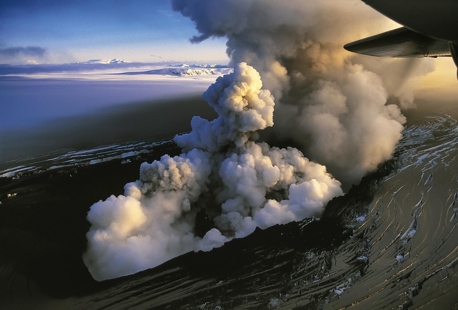 Ash and gas plume rising from a glacier covered with black ash