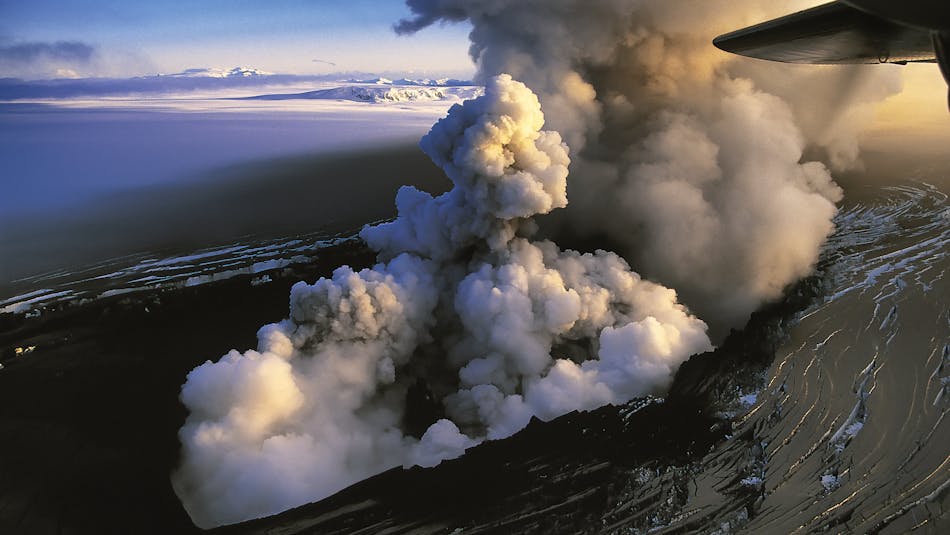 Ash and gas plume rising from a glacier covered with black ash